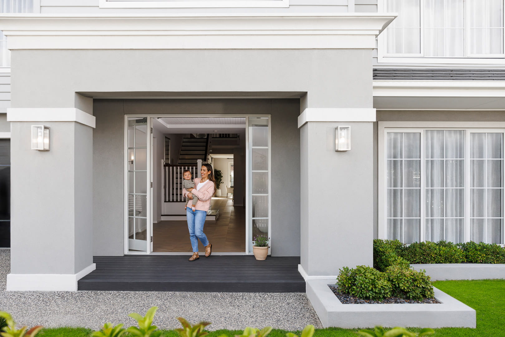 A young mother stands in the doorway of her Smiths Lane Clyde North home carrying her toddler in her arms.